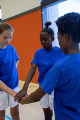 Diverse teen athletes stacking hands together in gym on floor wearing blue shirts and shorts