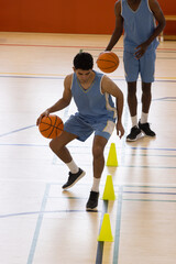 Obraz premium Diverse male teammates in blue jerseys practicing dribbling on court with basketball and cones