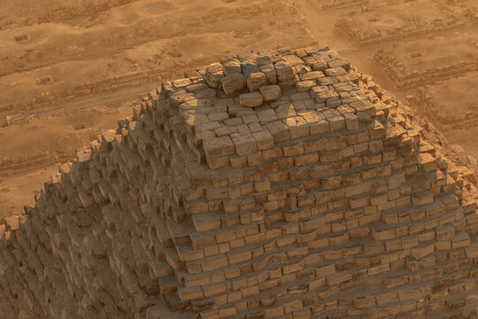 Aerial view of the weathered peak of an ancient pyramid, its stone blocks bathed in the warm glow of the desert sun, Giza, Egypt.
