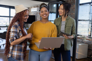 Diverse female colleagues collaborating around laptop and tablet in modern open-plan office space