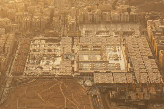 Aerial view of the magnificent Masjid an Nabawi casting shadows on the pale ground, surrounded by symmetrical buildings, Madinah, Al Madinah Province, Saudi Arabia.