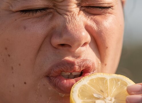 Funny portrait of person making sour face expression after eating fresh lemon slice showing scrunched eyes and wrinkled nose reaction