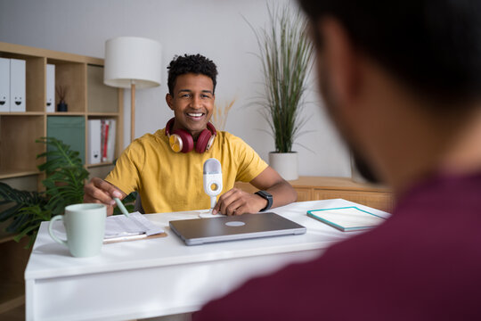 Smiling man interviewing at desk with microphone and laptop indoors