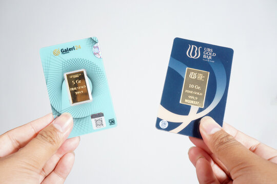 a man is holding a 5g gold bar from gallery24 and a 3g from ubs gold on a isolated white background