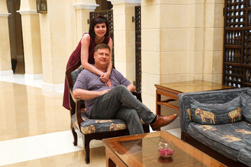 woman hugs man sitting in a chair.