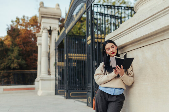 Woman reading notebook while leaning on stone wall at Retiro Park Madrid