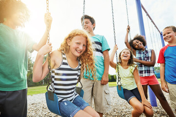 Happy, playing and group of children on swings at park with fun, bonding and development together. Portrait, flare and kids friends with smile on playground for growth, game or summer holiday.