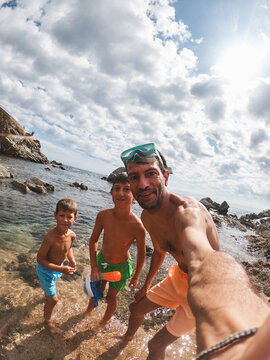 Father and two sons taking selfie on rocky beach with snorkel gear