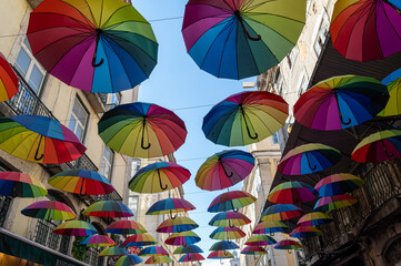 Brightly colored umbrellas are suspended above a lively street under a clear blue sky.