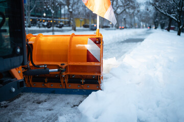 Orange snow plow clearing street after winter blizzard