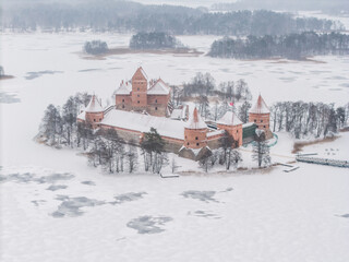Aerial view of the striking red-brick Trakai Island Castle stands proudly amidst the frozen expanse of Lake Galve, a stark contrast to the surrounding snow-laden landscape, Trakai, Lithuania.