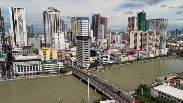 Aerial view over Pasig River bridge and dense Manila skyline with high rise towers and waterfront blocks near historic districts under cloudy daylight