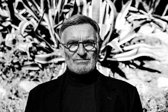 Serious man in glasses wearing trench coat outdoors in black and white