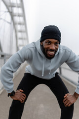 Athletic man resting in squat position during outdoor workout on a pedestrian bridge. Focused cardio training, urban fitness routine, strength and endurance exercise, active lifestyle
