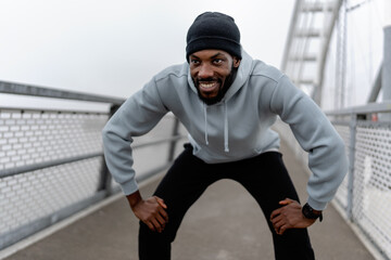 Athletic man resting in squat position during outdoor workout on a pedestrian bridge. Focused cardio training, urban fitness routine, strength and endurance exercise, active lifestyle