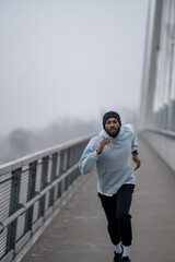 Athletic man running fast on a pedestrian bridge during outdoor workout. Urban cardio training, speed and endurance exercise, focused fitness routine and healthy active lifestyle