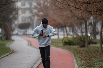Man in sportswear checking a smartwatch while jogging on a red running track in a foggy park. Outdoor fitness, cardio training, technology in sport, and healthy lifestyle concept