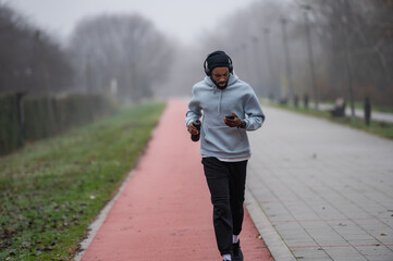 Man jogging on a red running track in a misty park, wearing a hoodie and sportswear. Outdoor fitness, healthy lifestyle, and endurance training on a foggy autumn or winter morning
