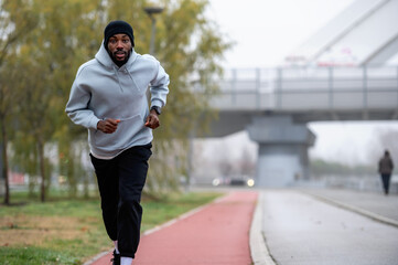 Man jogging on a red running track in a misty park, wearing a hoodie and sportswear. Outdoor fitness, healthy lifestyle, and endurance training on a foggy autumn or winter morning