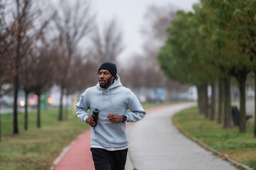 Man jogging on a red running track in a misty park, wearing a hoodie and sportswear. Outdoor fitness, healthy lifestyle, and endurance training on a foggy autumn or winter morning