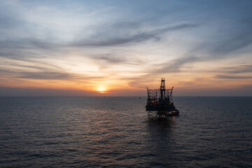 Fototapeta premium Aerial view from a drone of big jack up offshore drilling oil rig, production platform and supply vessel In the ocean during sunset - Oil and Gas Industry