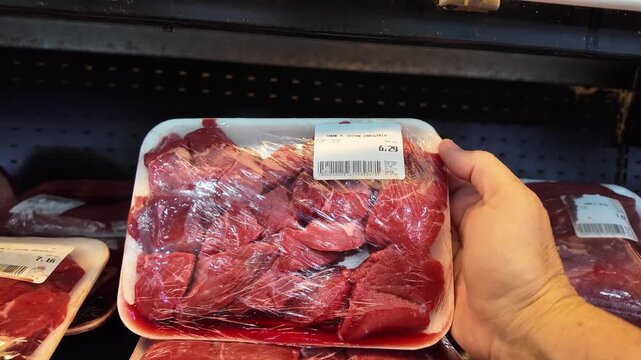 Close-up plastic-wrapped tray of carne de guisar raw beef displayed on refrigerated shelf in supermarket. Fresh red meat cuts food packaging, dolar pricing label, and everyday grocery shopping