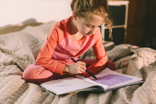 Child sitting on bed drawing in sketchbook at home