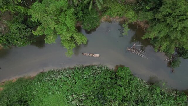 A detailed top-down aerial shot of a single traditional bamboo raft carrying tourists. The raft is being guided around a sharp bend in the Sok River, surrounded by dense, lush tropical jungle vegetati