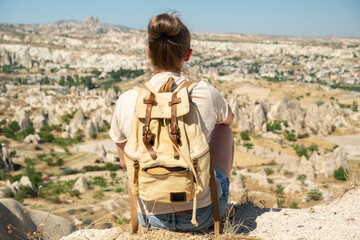 Person with backpack looks at landscape in Cappadocia while sitting on a hill during sunny day in summer