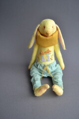 Toy rabbit figure sitting on a grey background wearing colorful clothes and soft scarf