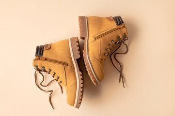 Stylish youth children's yellow men's boots made of genuine leather with laces on beige background top view. Rough-soled boots, work shoes, travel footwear. Stylish nubuck shoes