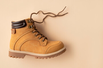 Stylish youth children's yellow men's boots made of genuine leather with laces on beige background top view. Rough-soled boots, work shoes, travel footwear. Stylish nubuck shoes