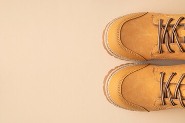 Stylish youth children's yellow men's boots made of genuine leather with laces on beige background top view. Rough-soled boots, work shoes, travel footwear. Stylish nubuck shoes