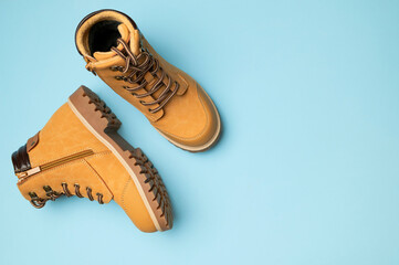 Stylish youth children's yellow men's boots made of genuine leather with laces on blue background top view. Rough-soled boots, work shoes, travel footwear. Stylish nubuck shoes