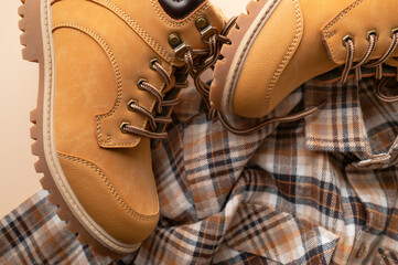 Fashionable clothes for child, boy, teenager. Yellow boots made of genuine leather nubuck, plaid shirt on beige background. Rough autumn-winter work boots with ribbed sole and laces 