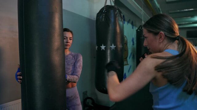 Two female boxers practicing punches on a punching bag.. two female boxers learn to punch a punching bag.