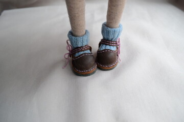 Feet in brown shoes with blue socks on a white background showing a close-up view of doll-like appearance