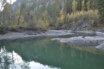 Quiet river flows through wooded area with autumn colors and rocky banks during late afternoon