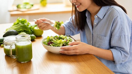 Woman eating salad at table with green smoothies