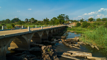 Aerial view of a concrete bridge with arched supports spans a rocky riverbed under a clear blue sky, Derre, Zambezia Province, Mozambique.