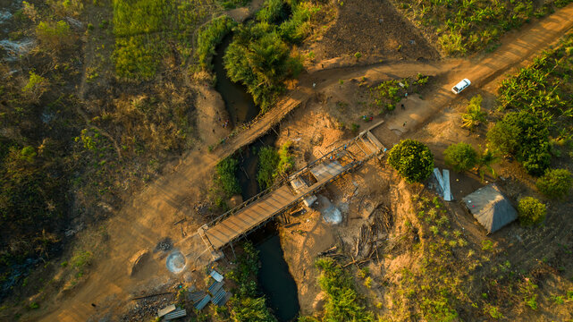 Aerial view of a wooden bridge spanning a narrow river, the landscape painted in hues of gold and green under the sun's embrace, Derre, Zambezia Province, Mozambique.