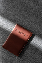 Brown leather passport cover on textured fabric in soft sunlight, minimalist travel document still life with copy space