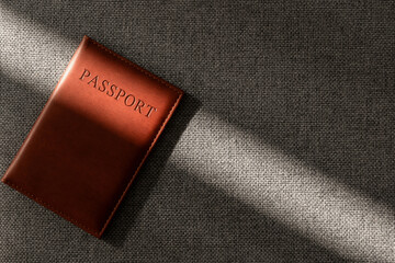 Brown leather passport cover on textured fabric in soft sunlight, minimalist travel document still life with copy space