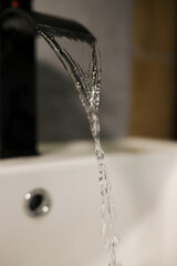 Close-up of the cleaning process: a hand holds a yellow sponge with detergent and cleans the black faucet and the surface of the sink. In the background is a bottle of household chemicals. The concept