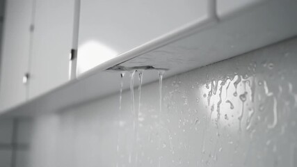 Urgent household plumbing issue with water leaking vigorously from an overhead cabinet, causing visible moisture and potential damage, requiring immediate professional repair