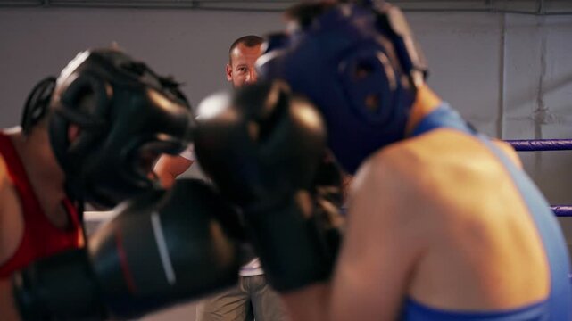 A fight between two boxers is supervised by a coach.. two young boxers have a fight in the ring under the guidance of a trainer.