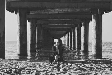 Young woman sitting on Baltic Sea beach under pier in calm contemplative mood