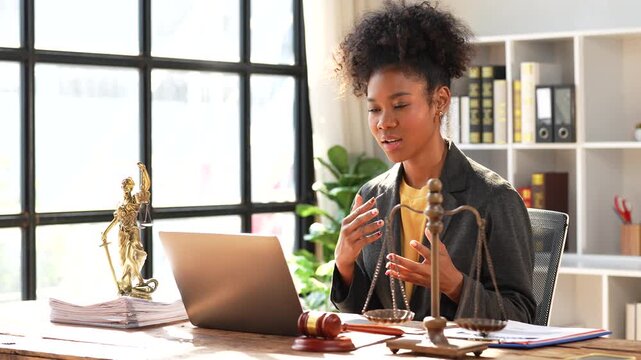 Professional african american female lawyer sitting at her desk in a modern law office, giving legal advice to a client during a video conference call on her laptop computer