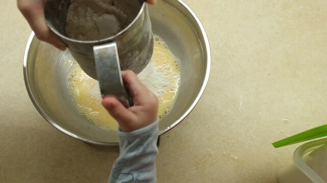 Sifting Flour into Mixing Bowl with Eggs Father hand with Toddler hand