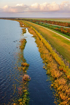Aerial view of the sun kissing the water's edge where the water meets the grassy bank, a symphony of blues and golds under a soft sky, Lake Okeechobee, Florida, United States.